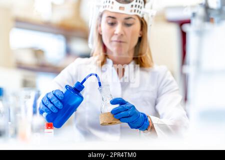 Una donna conduce ricerche sulle sostanze chimiche pericolose nel laboratorio biochimico dell'Istituto Scientifico. Utilizzare dispositivi di protezione, vetro Foto Stock