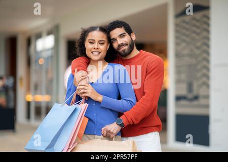 Coppia mediorientale che abbraccia le borse per lo shopping in piedi presso il centro commerciale Foto Stock