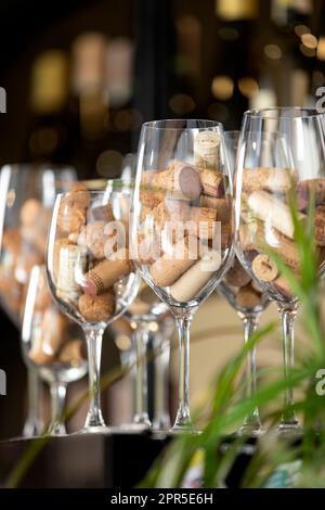 Fila di bicchieri da vino su un bar con tappi di bottiglie di vino al loro interno. Foto Stock