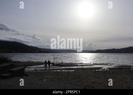 Bianco tramonto aprile al Lago inferiore di Costanza. Di fronte ad esso le piccole sagome di due bambini che giocano nel delta argenteo dell'estuario di Feldbach. Foto Stock