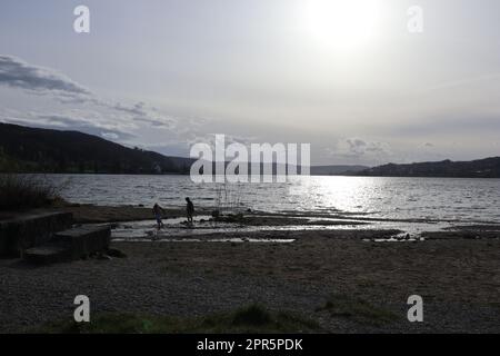 Bianco tramonto aprile al Lago inferiore di Costanza. Di fronte ad esso le piccole sagome di due bambini che giocano nel delta argenteo dell'estuario di Feldbach. Foto Stock