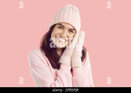 Donna brunetta sorridente in cappello e guanti a maglia, felpa rosa su sfondo rosa. Foto Stock