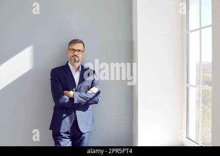 Uomo d'affari di mezza età seduto al muro con le mani ripiegate Foto Stock