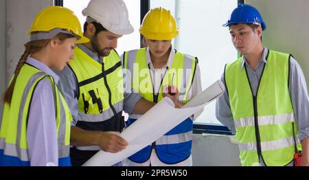 Il giovane caposquadra asiatico con casco blu e giubbotto di sicurezza ha cercato di assistere per guardare il piano di costruzione. Ambiente di lavoro nel cantiere di progetto di edilizia abitativa. Foto Stock