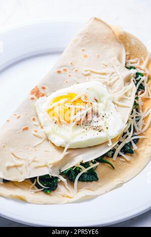 pancake farcito con foglie di spinaci servito con uova fritte e formaggio grattugiato Foto Stock