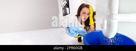 Donna che guarda Sink Pipe Leakage in Kitchen Foto Stock