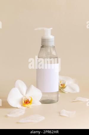 Un flacone erogatore a pompa vicino ai fiori di orchidea bianchi su un primo piano di colore giallo chiaro. Mockup Foto Stock