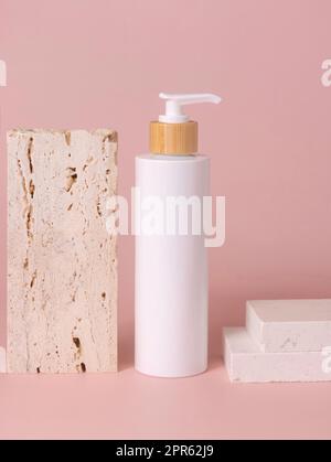 Una bottiglia bianca vicino alla pietra beige con primo piano rosa chiaro, Mockup Foto Stock