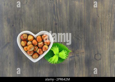 Nocciole fresche non sgusciate in un piatto a forma di cuore Foto Stock