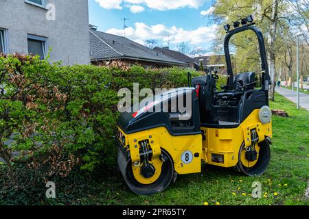 A small road-building roller of yellow-black color standing on the lawn near the house. Foto Stock