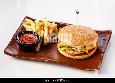 Hamburger. Succosa cotoletta di maiale, formaggio cheddar, cipolle sottaceto croccanti, lattuga avvolta in un panino sotto due salse. Servito con patatine fritte Foto Stock