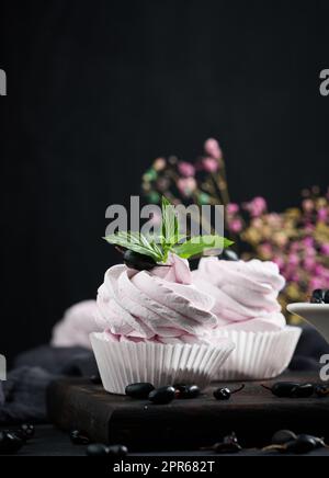 Marshmallows di frutta porzionati in una tazza di carta su un asse di legno nero Foto Stock