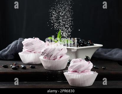 Marshmallows di frutta porzionati in una tazza di carta su un asse di legno nero Foto Stock