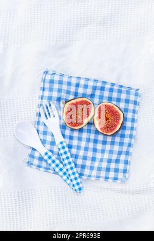 I fichi freschi biologici maturi tagliati in due parti si trovano su un tovagliolo a scacchi blu. Preparazione dei fichi per la preparazione dell'inceppamento. Piatto autunnale. Spazio libero per il testo. Foto Stock