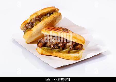 Panini Street food con carne, cetrioli sottaceto su un piatto bianco. Sfondo bianco. Vista laterale. Foto Stock