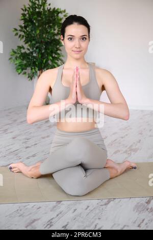 Ritratto di una giovane donna che medita in studio mentre si siede in una posizione di mezzo loto su un tappeto yoga. Foto Stock