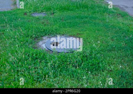 tombino in ghisa rotto tra l'erba del parco. Tombino con foro Foto Stock