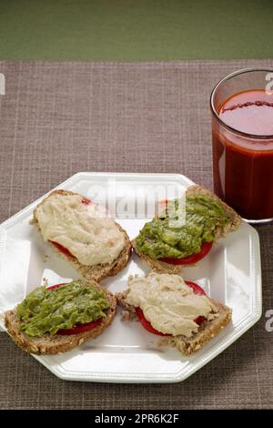 Guacamole, pomodoro, Hummus su pane germogliato con succo di verdure Foto Stock