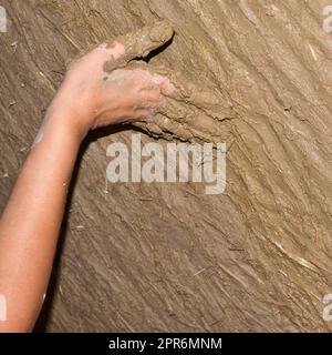 Mano di una giovane donna che costruisce un muro ecologico con argilla e gesso di paglia. Edificio con materiale naturale Foto Stock