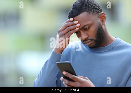 Un uomo nero preoccupato che controlla il telefono per strada Foto Stock