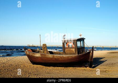 Sulla spiaggia di sabbia si trova una piccola barca da pesca in legno sul mare Foto Stock