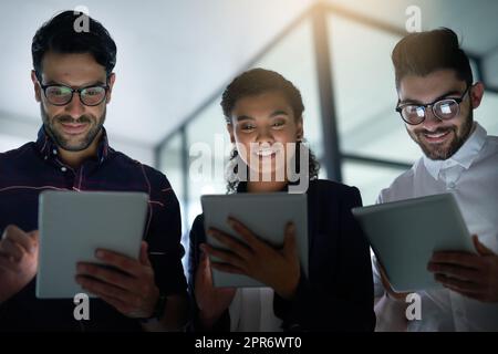 Tecnologia coinvolgente in team. Immagine di tre colleghi che utilizzano tablet digitali mentre si trovano in ufficio. Foto Stock