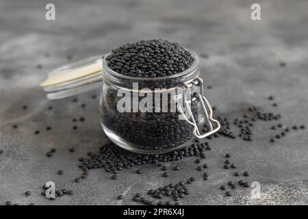 Vaso di vetro di lenticchie nere secche fagioli su tavolo grigio primo piano, dieta proteica sana Foto Stock