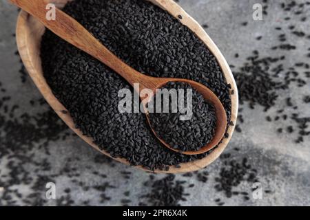 Spezie indiane cumino nero (nigella sativa o kalonji) semi in ciotola con cucchiaio su tavola di legno vista dall'alto. Foto Stock