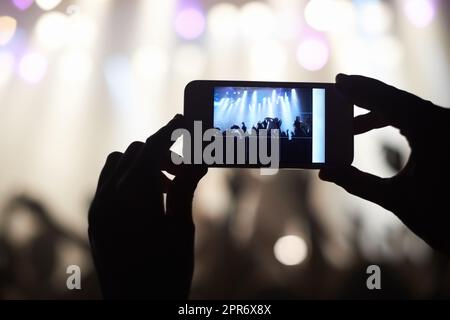 Una persona che filma la propria band preferita con un telefono con fotocamera. Questo concerto è stato creato per il solo scopo di questo servizio fotografico, con 300 modelli e 3 gruppi dal vivo. Tutte le persone in questa foto sono state rilasciate. Foto Stock