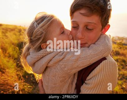 Un abbraccio per il suo eroe. Scatto corto di una bambina che dà a suo fratello un bacio sulla guancia mentre all'aperto. Foto Stock