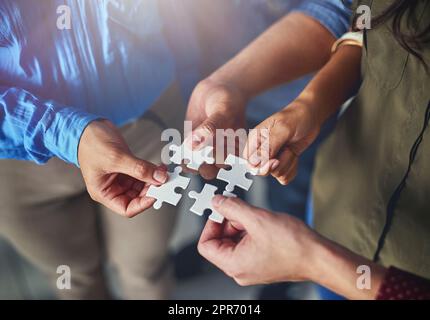 Trovare le soluzioni giuste in team. Colpo di un team di uomini d'affari che mette insieme pezzi puzzle in un ufficio. Foto Stock