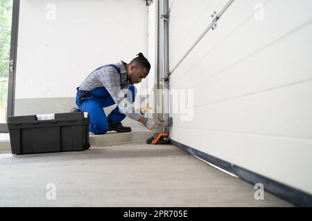 Installazione e riparazione della porta del garage a casa. Uomo appaltatore Foto Stock