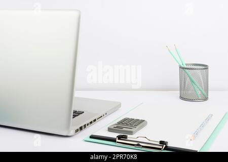 LAP Top, Appunti vuoti con carta, tazza con matite e calcolatrice in ufficio. Scrivania con computer, notebook vuoto e scatola con penne. Cancelleria sul posto di lavoro. Foto Stock