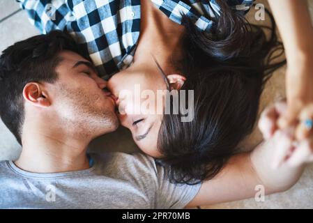 Cucina piano baci sono i migliori baci. Scatto di una giovane coppia felice che riposa sul pavimento mentre si sposta nella loro nuova casa. Foto Stock