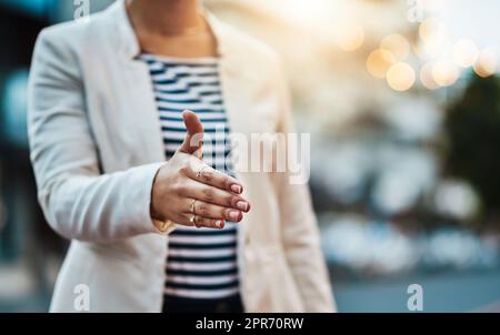 Fare affari in tutta la città. Primo piano di un'irriconoscibile donna d'affari che estende una stretta di mano in città. Foto Stock