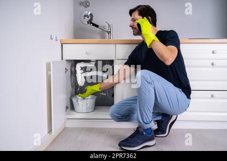 Sad Young Man Calling Plumber in Front of Water Leaking Foto Stock