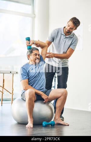 Qualsiasi disagio. Shot completo di un giovane fisioterapista maschile che assiste un paziente anziano in guarigione. Foto Stock