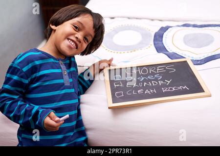 Controllare le attività. Ritratto di un giovane ragazzo che tiene una lavagna con le faccende scritte. Foto Stock