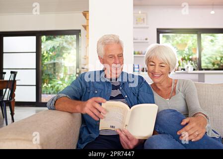 Tra le pagine di un libro d'amore. Scatto di una coppia senior rilassata che legge un libro insieme sul divano a casa. Foto Stock