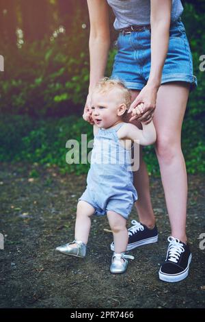 Oggi cammina, domani corre. Shot di una ragazza adorabile bambino imparare a camminare con l'aiuto di sua madre all'aperto. Foto Stock