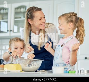Famiglia felice amorevole stanno cuocere insieme. Madre e due figlie cucinano biscotti e si divertono in cucina. Cibo fatto in casa e piccolo aiutante. Foto Stock