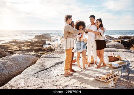 Un gruppo di amici che si divertono insieme e festeggiano con delle bevande alcoliche in spiaggia Foto Stock