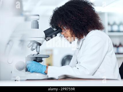 Uno scienziato di razza mista con capelli ricci che indossa occhiali di sicurezza e guanti che analizza campioni di test medici su un microscopio in laboratorio. Giovane donna che fa ricerche forensi e sperimenta per sviluppare una cura Foto Stock