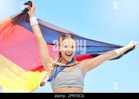 Ritratto dell'atleta vincente che tira la bandiera tedesca dopo aver gareggiato in sport. Vestibilità sorridente donna attiva sportiva motivata. Festeggiamo il conseguimento della medaglia d'oro nello sport olimpico con orgoglio nazionale Foto Stock