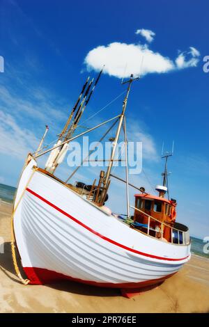 Splendido paesaggio di una barca da pesca bianca parcheggiata sulla spiaggia in una giornata di sole. Barca da pesca su una spiaggia sabbiosa. Una barca da pesca locale ormeggiata sulla riva su una bella e luminosa barca di legno sulla spiaggia Foto Stock