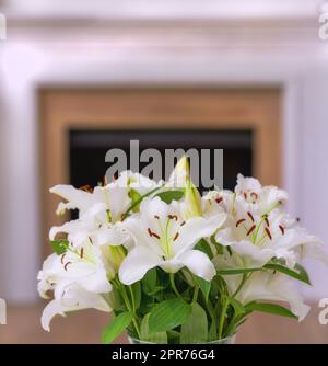 Primo piano di un bouquet di fiori di giglio in un vaso su un tavolo a casa. Mazzo di piante bianche in fiore al Lilio che fioriscono in un vaso nel soggiorno. Gigli in mostra in un'imbarcazione nel salotto di una casa Foto Stock