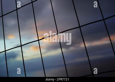 Primo piano di una recinzione di filo al tramonto. Sfondo di linee verticali e orizzontali. Silhouette di rete metallica a forma di rettangolo per un concetto di sicurezza. Foto Stock