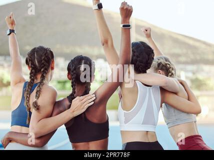 Vista posteriore di fieri campioni olimpici che si abbracciano e tifanno insieme in unità. Squadra giovane attiva che si rallegra dopo aver vinto un risultato. Un gruppo di diverse atlete che celebrano la vittoria. Foto Stock