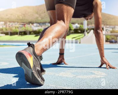 Primo piano di un atleta che si prepara a correre in pista e in campo con i piedi sui blocchi di partenza pronti per iniziare a correre. Primo piano di un uomo in posizione di partenza per una gara su una pista sportiva Foto Stock