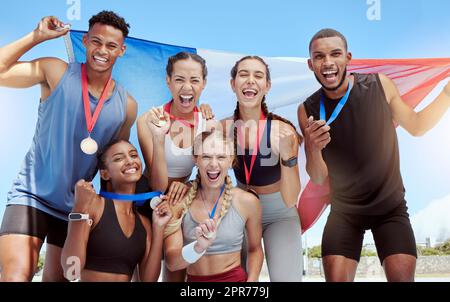 Atleti olimpici francesi felici e orgogliosi che festeggiano la vittoria di medaglie per il loro paese. Ritratto di un gruppo eterogeneo di sportivi con una bandiera francese, esultante e orgoglioso del loro successo e vittoria Foto Stock